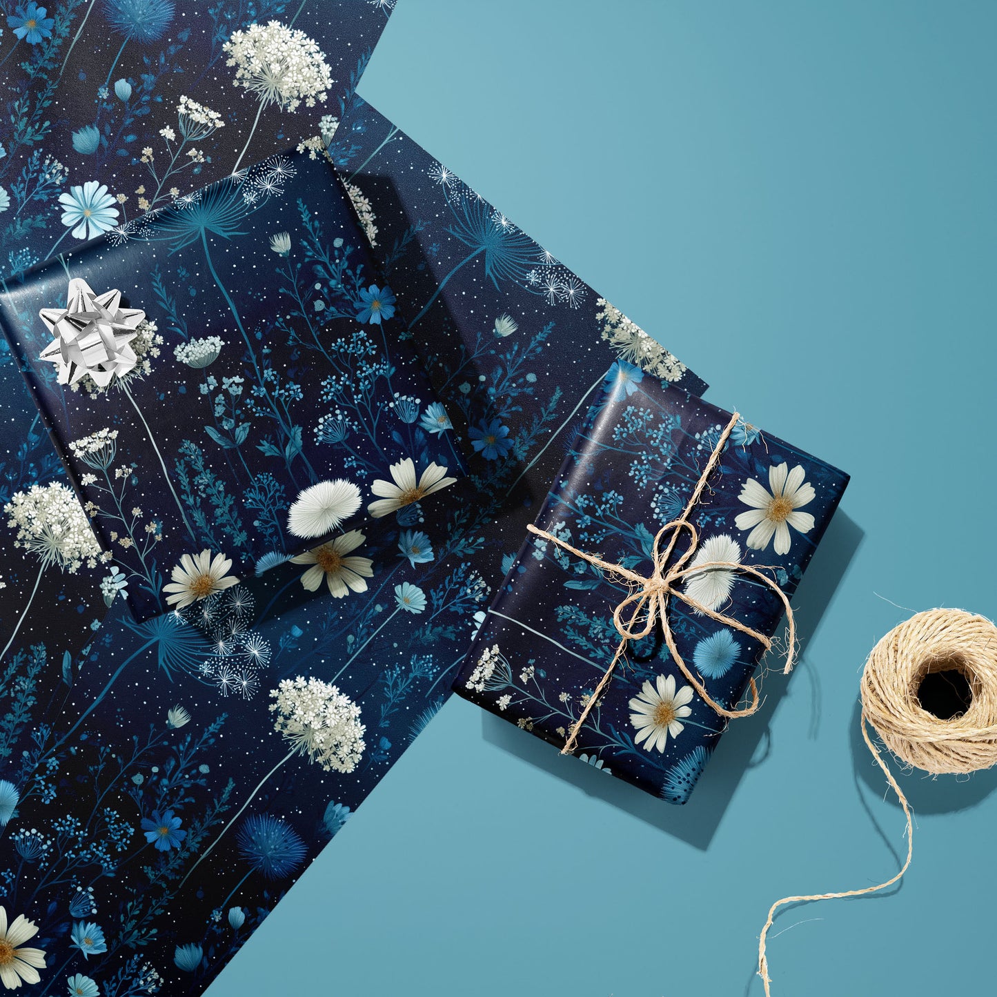 Two gifts in Midnight Garden wrap—one with a silver bow, one tied with twine—rest on two unused sheets beside a spool of twine on a teal background.