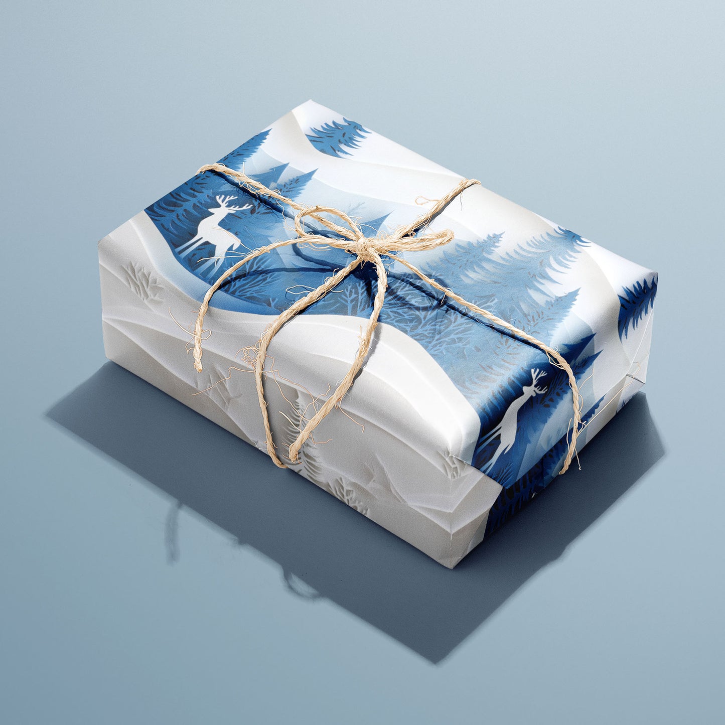 A single gift wrapped in Alpine Serenity and tied with natural twine, revealing alpine mountains, evergreens, and starlight on a deep blue ground, set on a cool slate-blue surface.