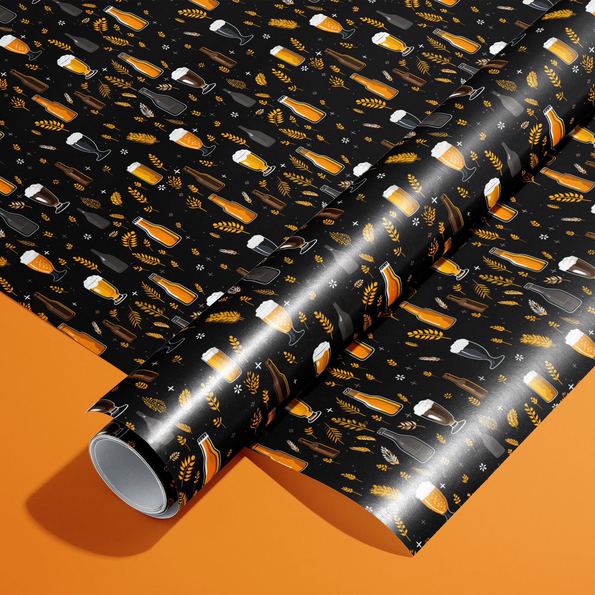 A roll on an unrolled sheet of Midnight Hops wrapping paper featuring beer mugs, bottles, pint glasses, hops, and barley on black, set on a vivid orange background.
