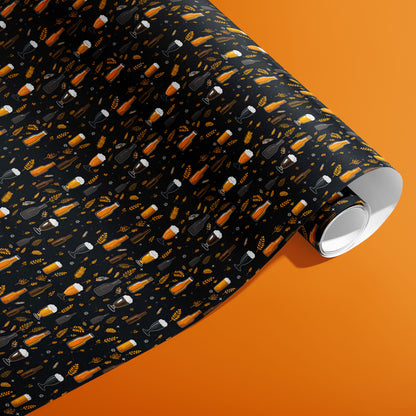 A partially unfurled roll of Midnight Hops wrapping paper showing frothy beer glasses, bottles, and barley sprigs on black against an orange background.