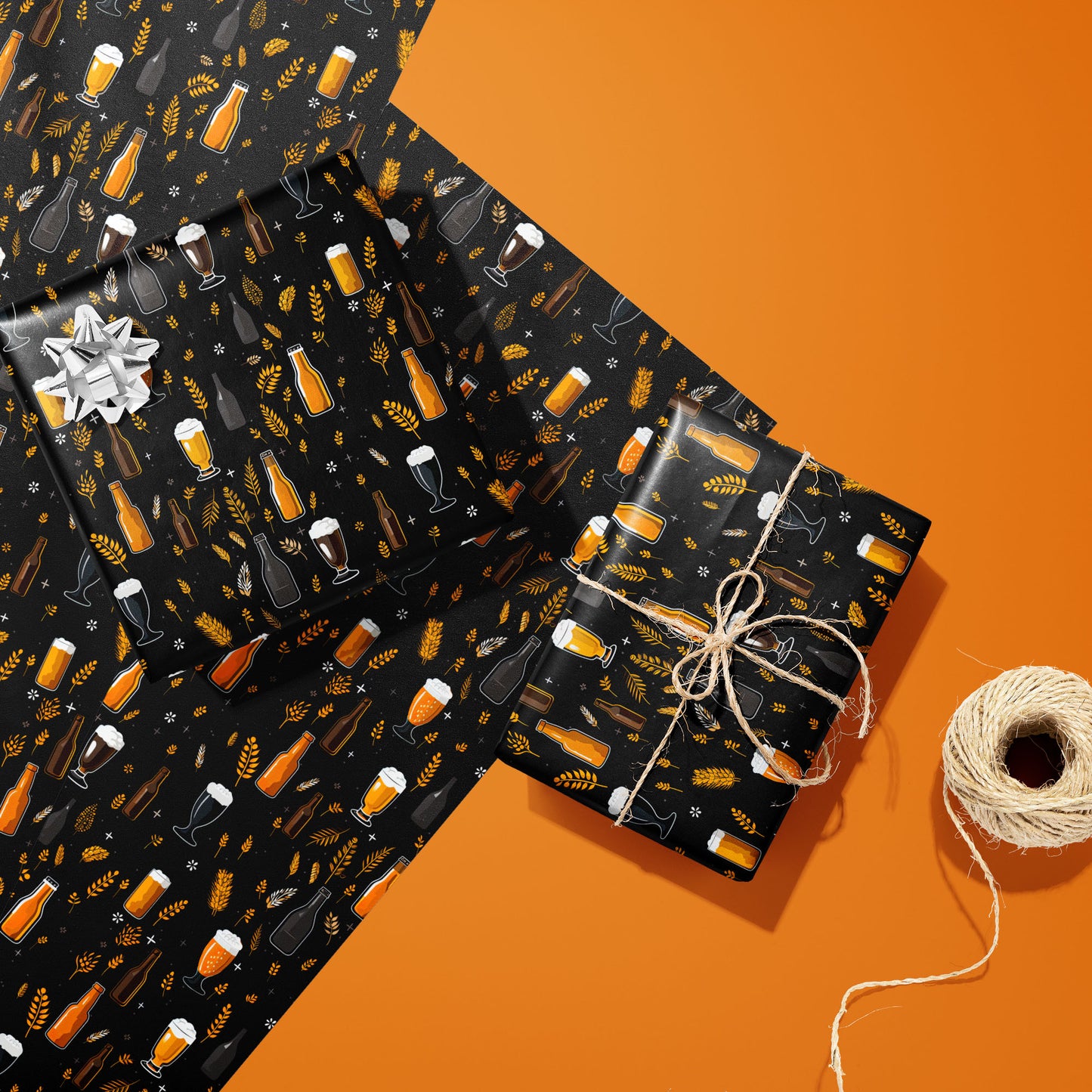 Two gifts in Midnight Hops wrap—one with a silver bow and one tied with twine—rest on two unused sheets beside a spool of twine on an orange background.