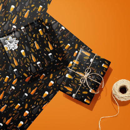 Two gifts in Midnight Hops wrap—one with a silver bow and one tied with twine—rest on two unused sheets beside a spool of twine on an orange background.