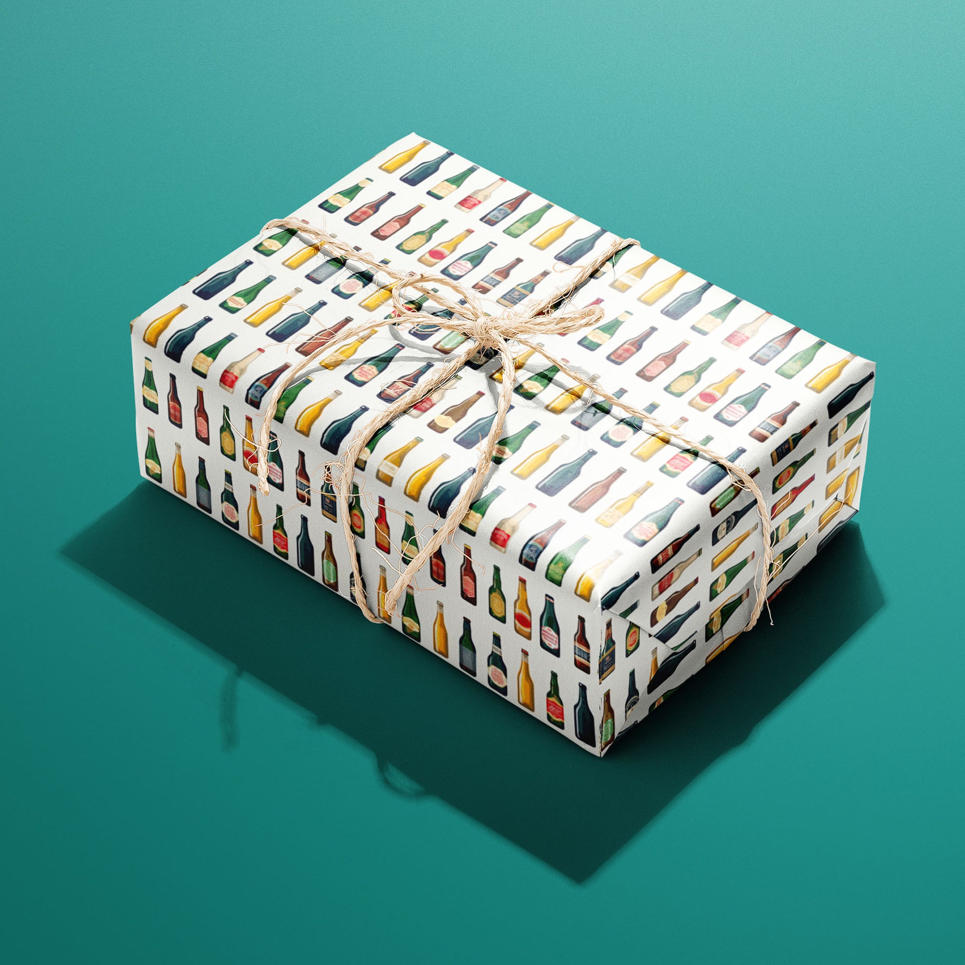 A single rectangular gift wrapped in Artistic Ales and tied with natural twine highlights painterly beer bottles and frothy pints with hops and barley on a warm gray backdrop.