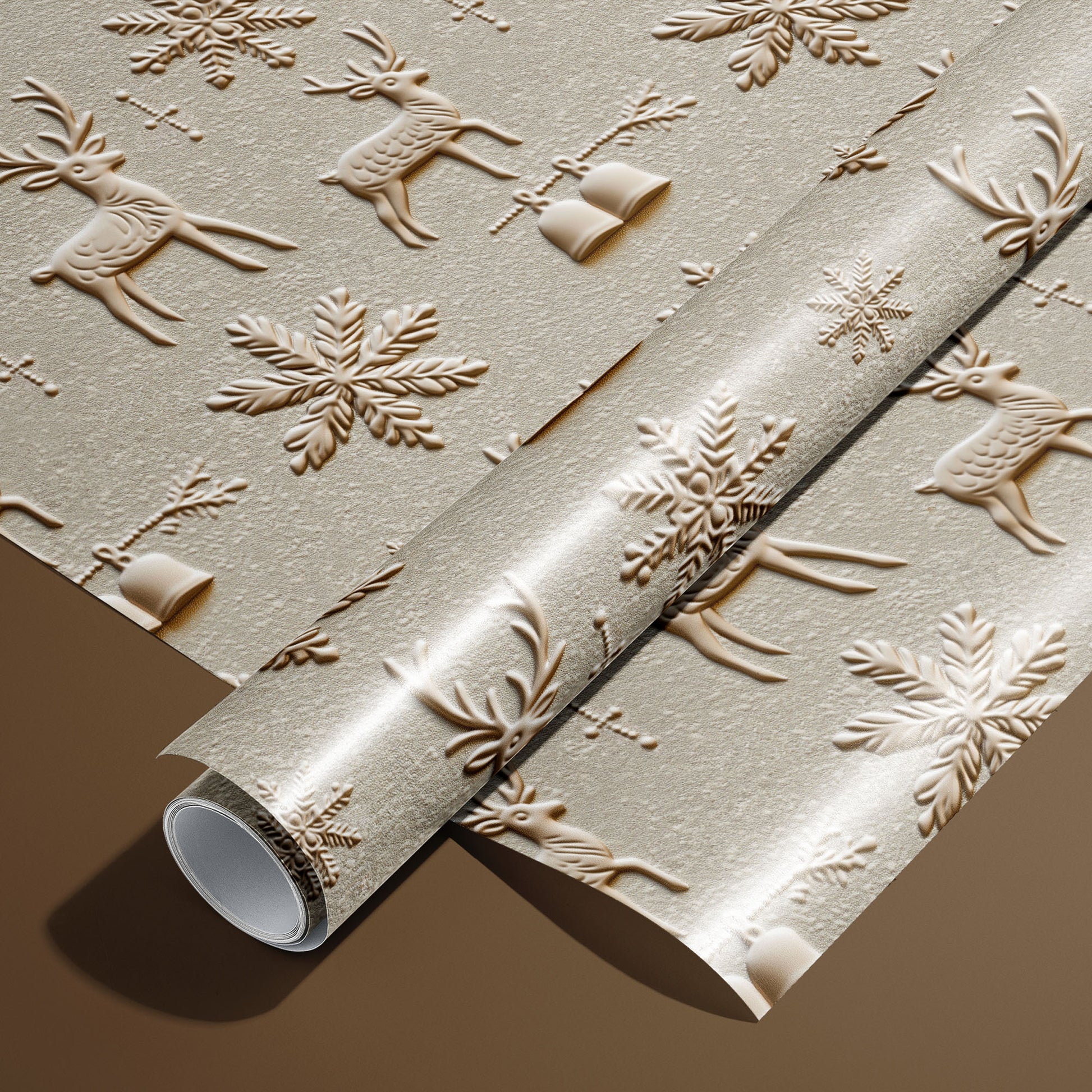 A roll of Winter Impressions wrapping paper on an unrolled sheet, featuring embossed-style reindeer, snowflakes, bells, and sprigs in warm taupe on a pale stone ground, on a warm brown surface.