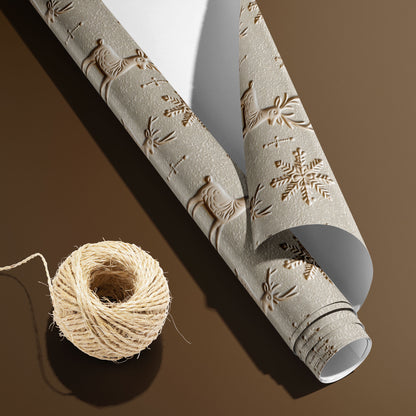 A partially unfurled roll of Winter Impressions with its white underside visible beside a spool of natural twine, featuring embossed-look reindeer and snowflakes on a pale stone ground over a warm brown surface.