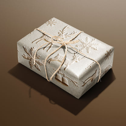 A single gift wrapped in Winter Impressions and tied with natural twine, displaying embossed-look reindeer, snowflakes, and bells on a pale stone ground, set on a warm brown surface.