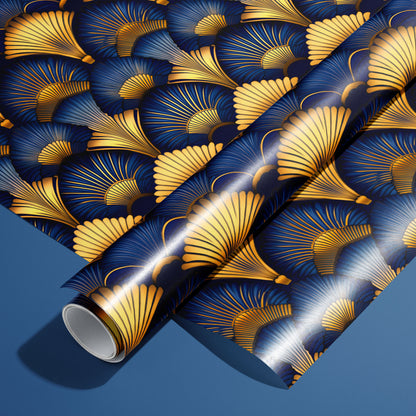 A roll of Gilded Ginko rests on a matching unrolled sheet, featuring gold and blue ginkgo leaves and fine stems, on a blue surface.