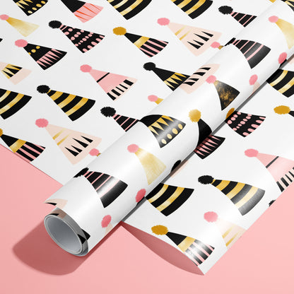 A roll on an unrolled sheet of Party Hat Parade wrapping paper with colorful party hat and pom-poms, set on a bright pink background.