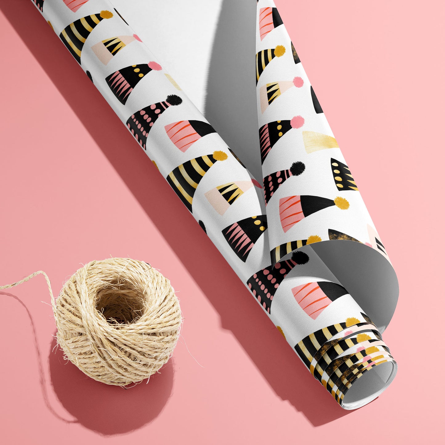 A partially unfurled Party Hat Parade roll with the white underside visible beside a spool of natural twine, featuring festive hats on a bright pink background.