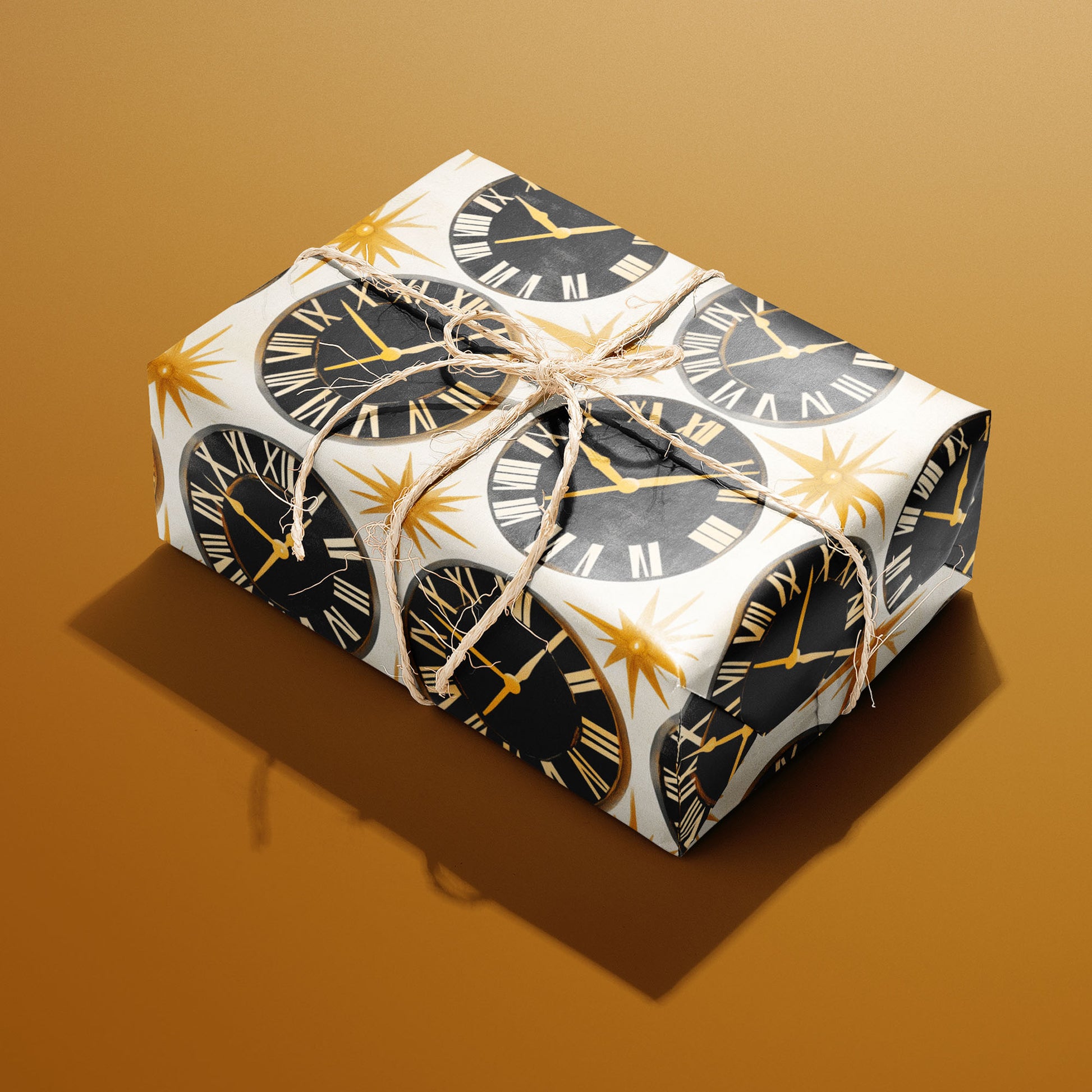 A rectangular gift wrapped in Deco Century paper and tied with natural twine features black clock faces and gold starbursts on pearl white against a golden mustard background.