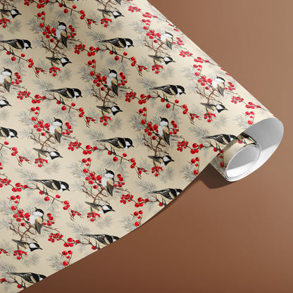 A partially unfurled roll of Bird & Berry wrapping paper reveals chickadees perched among red berries and pine on a cream ground against a warm brown background.