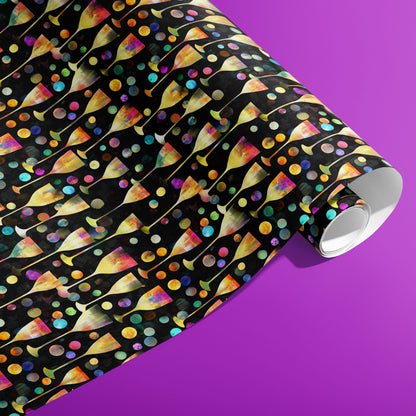 A partially unfurled roll of Radiant Revelry wrapping paper reveals iridescent champagne flutes with rainbow bubbles on black against a vibrant purple background.