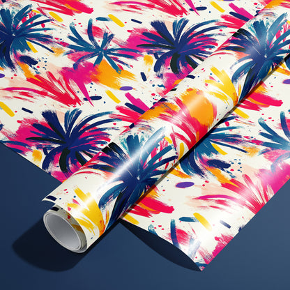 A roll of Artful Fireworks paper on a matching unrolled sheet shows painterly firework bursts with lively brushstrokes and splashes in magenta, cobalt, and gold on cream, resting on a navy blue surface.