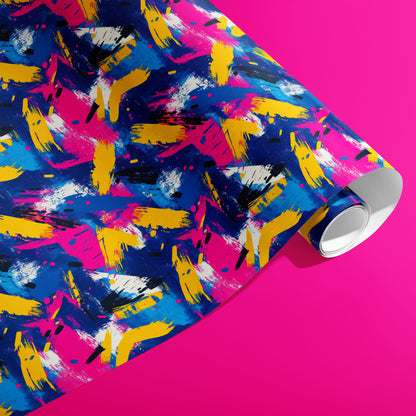 A partially unfurled roll of Electric Splash wrapping paper reveals neon brushstroke splashes in magenta, yellow, and cobalt with black dashes and white flecks on a hot pink background.