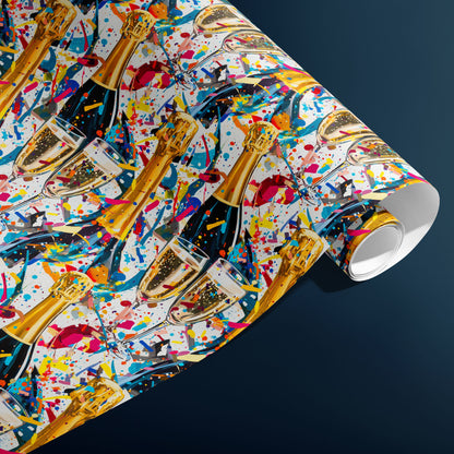 A partially unfurled roll of Glitter & Fizz wrapping paper reveals glittering confetti and bubbly motifs with champagne bottles and flutes on white, resting against a charcoal gray background.
