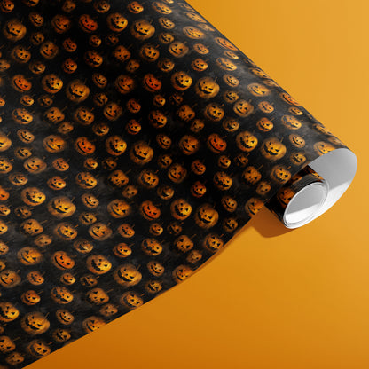 A partially unfurled roll of Jack-o-Lanterns wrapping paper reveals glowing carved pumpkins across a smoky black pattern, photographed on an orange background.