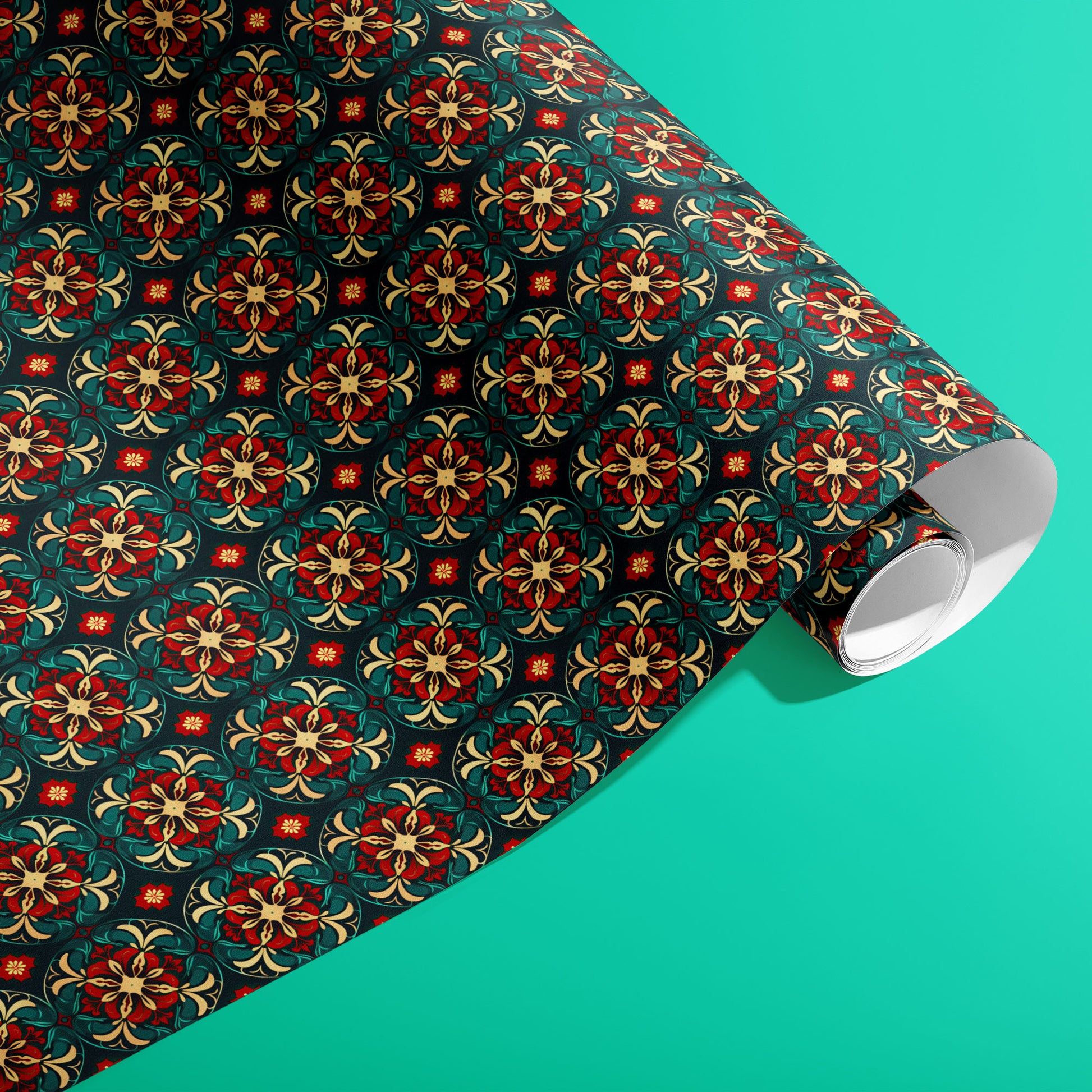 A partially unfurled roll of Arabesque Christmas giftwrap displaying ornate arabesque medallions in red, gold, and green on deep navy against a bright teal surface.