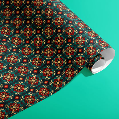 A partially unfurled roll of Arabesque Christmas giftwrap displaying ornate arabesque medallions in red, gold, and green on deep navy against a bright teal surface.