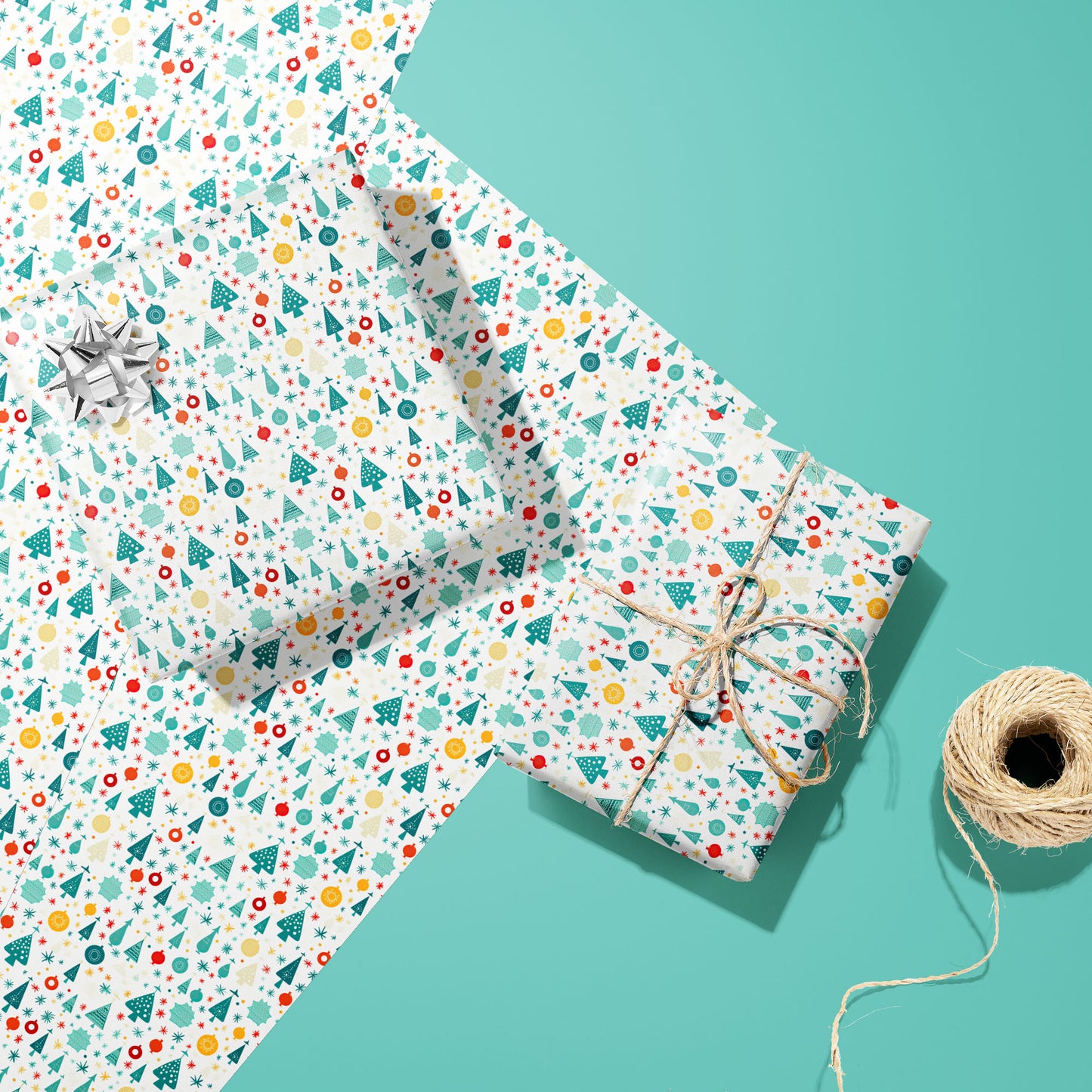 Two gifts wrapped in Childlike Christmas paper—one topped with a silver bow and one tied with natural twine—rest on two matching sheets beside a twine spool on a soft mint-green surface.