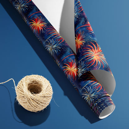 A partially unfurled roll of Blooming Sky with the white underside visible beside a spool of natural twine, featuring vibrant fireworks on a midnight navy print over a steel-blue surface.