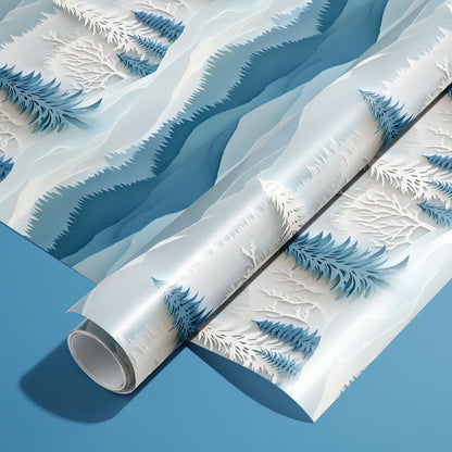 A roll on an unrolled sheet of Snowy Grove wrapping paper featuring layered paper-cut pines and frosted branches in icy blues and white, set on a medium blue background.