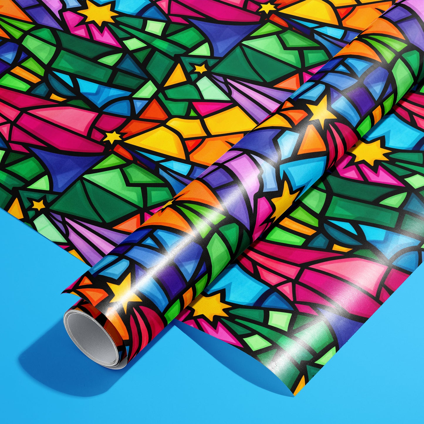 A roll of Christmas Kaleidoscope wrapping paper resting on a matching unrolled sheet, with stained-glass stars and kaleidoscopic shards in vivid hues on a bright blue background.