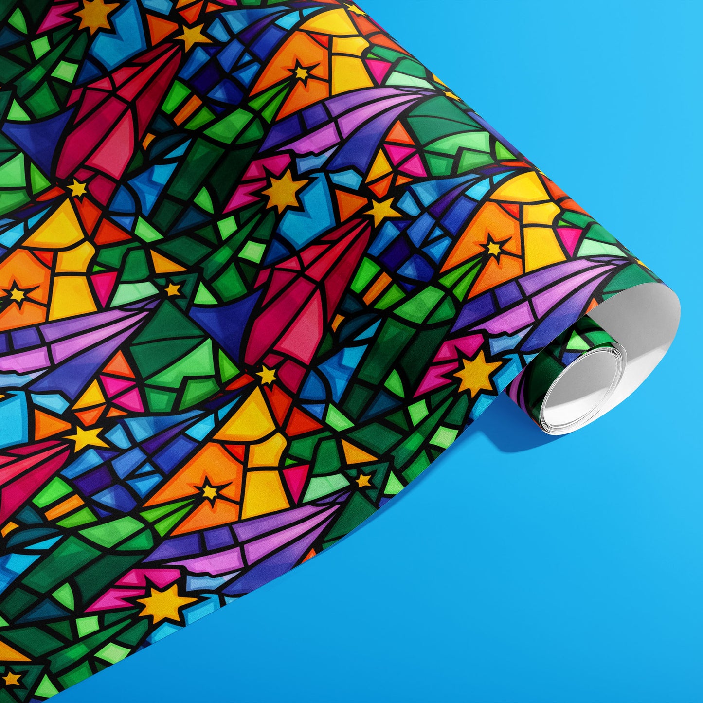 A partially unfurled roll of Christmas Kaleidoscope paper showcasing bold black-lined, stained-glass stars and comet shapes in saturated rainbow tones on a bright blue backdrop.