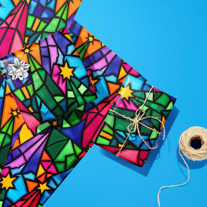 Two gifts in Christmas Kaleidoscope—one with a silver bow and one tied with natural twine—rest on two unused sheets beside a spool of twine on a bright blue background.