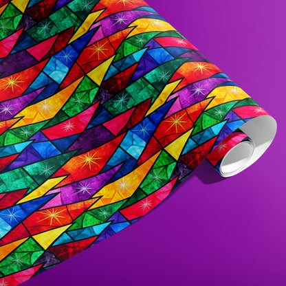 A partially unfurled roll of Prismatic Holiday wrapping paper featuring rainbow stained-glass facets and twinkling starbursts on a vibrant purple surface.