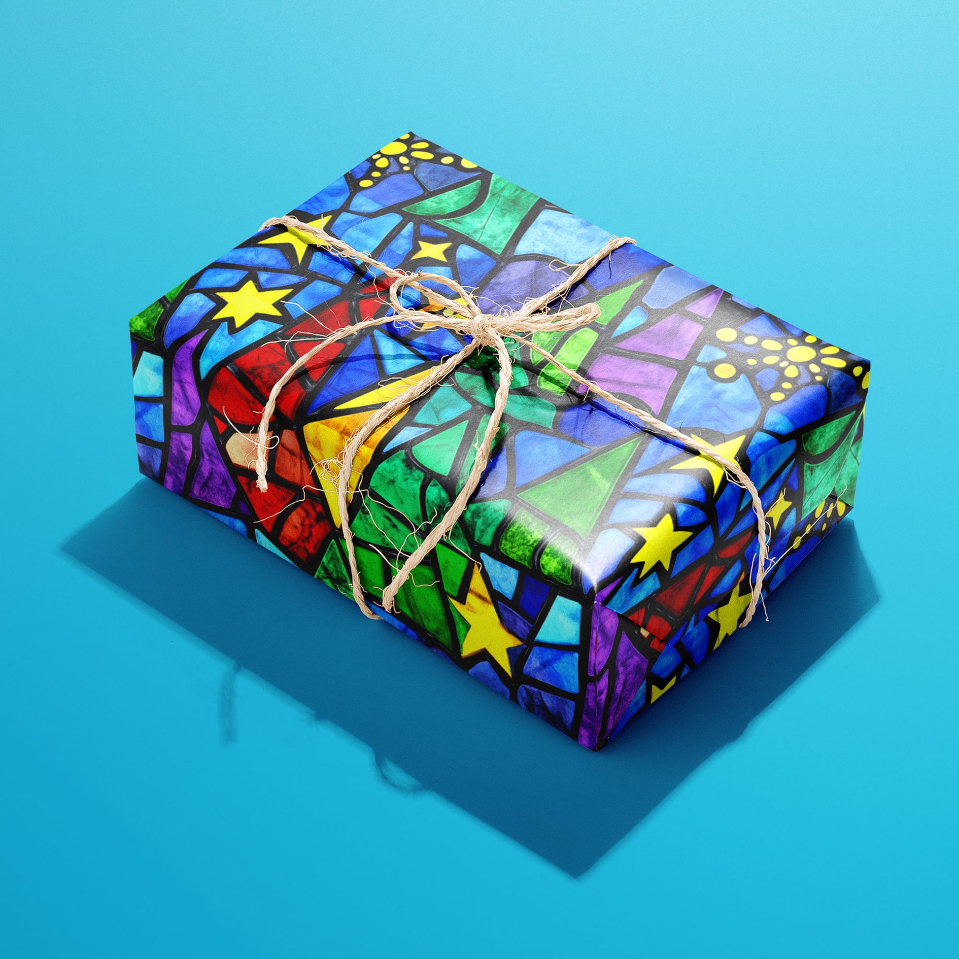A single rectangular gift wrapped in Starlit Holiday and tied with natural twine highlights stained-glass stars and stylized trees in jewel tones on a bright cyan backdrop.