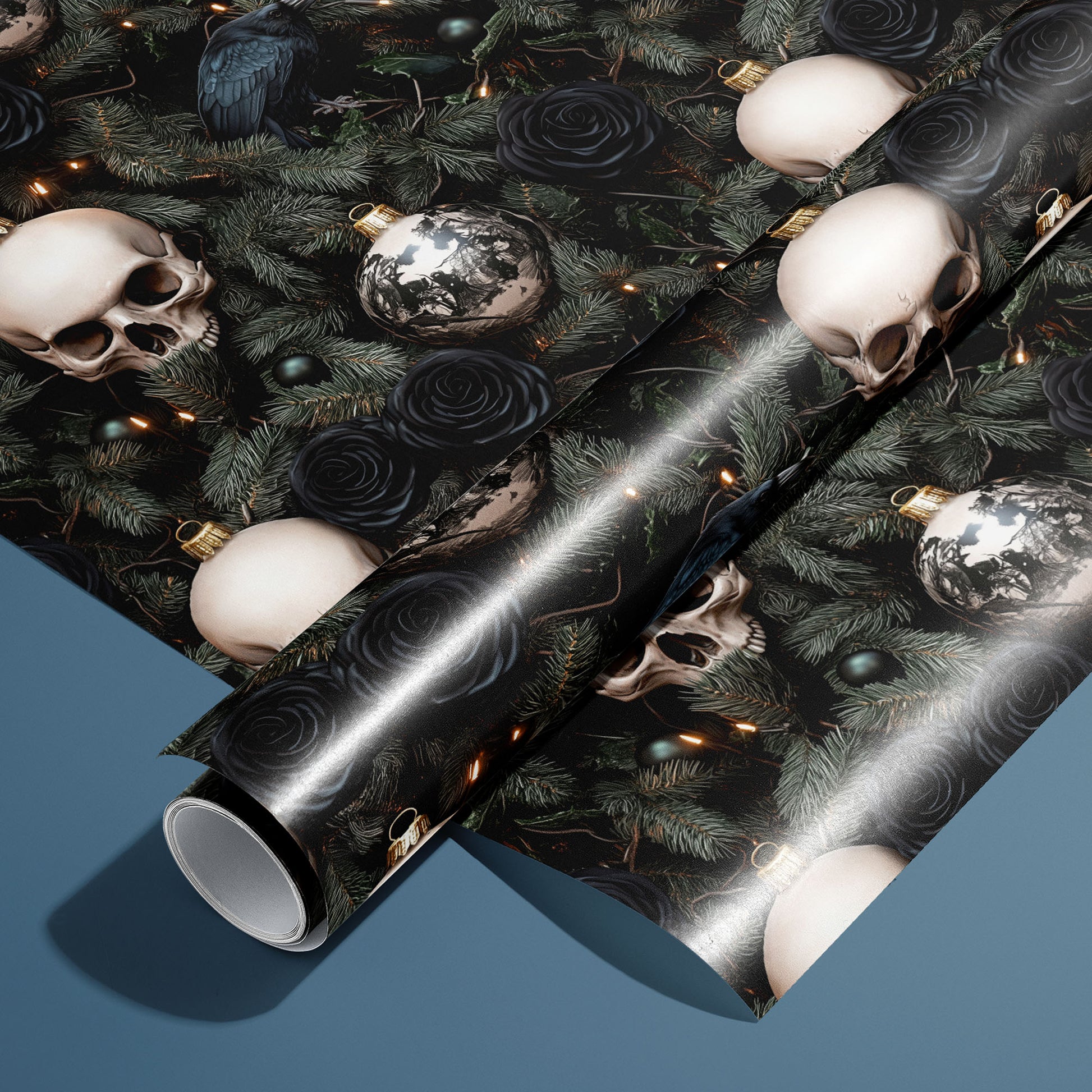 A roll of Dark Yuletide rests on a matching unrolled sheet, featuring skull ornaments, ravens, black roses, evergreen boughs, and warm fairy lights on a black ground over a steel blue surface.