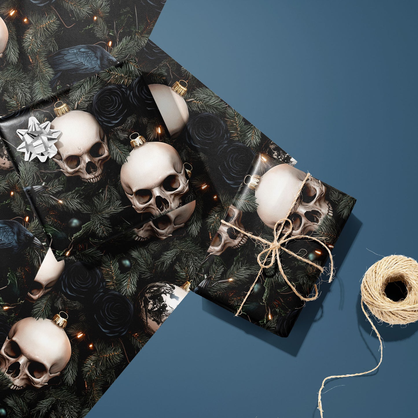 Two gifts in Dark Yuletide—one silver-bowed and one tied with twine—rest on two unused sheets with skull ornaments, ravens, and black roses beside a twine spool on steel blue.