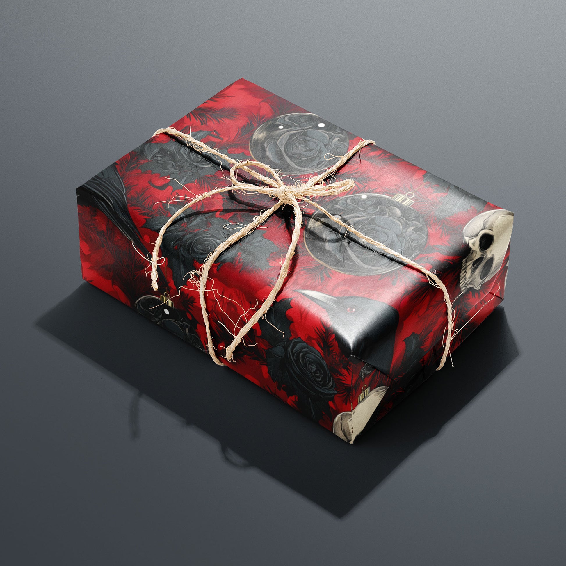 A single rectangular gift wrapped in Merry Macabre and tied with natural twine highlights ravens, skulls, and black roses over crimson foliage on a charcoal gray backdrop.