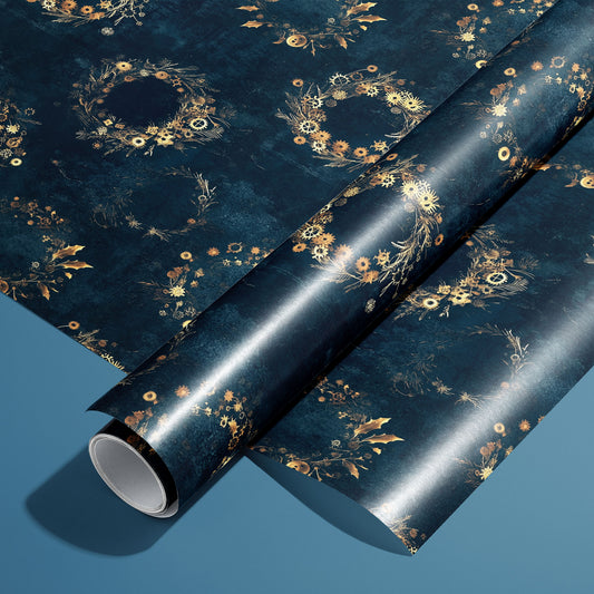 A roll of Gilded Gears wrapping paper rests on a matching unrolled sheet, showing steampunk wreaths of gilded cogs, holly, and pine on a deep navy background over a blue surface.