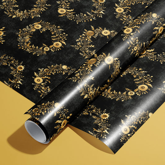 A roll of Clockwork Wreaths wrapping paper resting on a matching unrolled sheet, with gilded gear-and-foliage wreaths on charcoal black, set on a mustard-yellow surface.