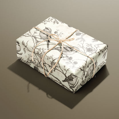 A single rectangular gift wrapped in Woodland Carols and tied with natural twine shows songbirds and pinecones on twiggy branches over a parchment-cream ground against a taupe backdrop.