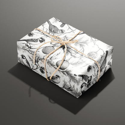 A single rectangular gift wrapped in Ornamental Nesting and tied with natural twine, the monochrome birds, ornaments, and pine boughs crisp on a white background over dark gray.