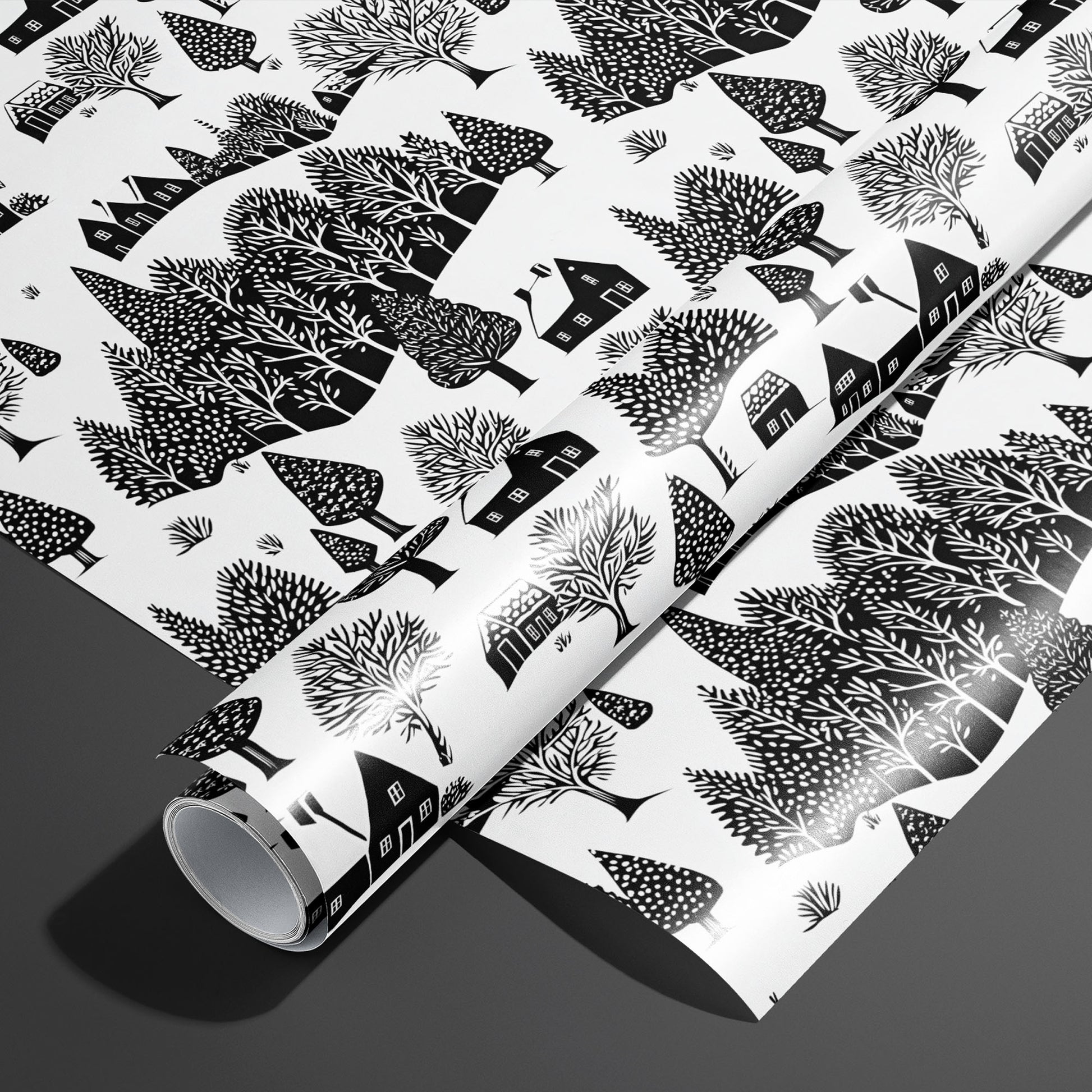 A roll of Snowbound Village on a matching unrolled sheet, featuring black silhouette houses and snowy trees on a crisp white background atop a dark gray surface.