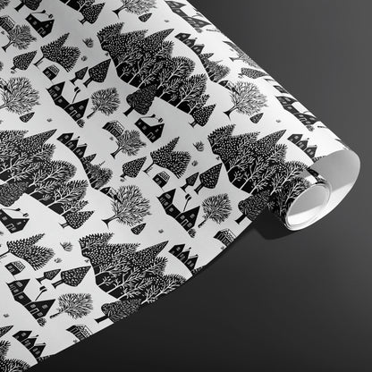 A partially unfurled roll of Snowbound Village showing cozy cottages and snow-dotted trees in black on white against a dark gray backdrop.