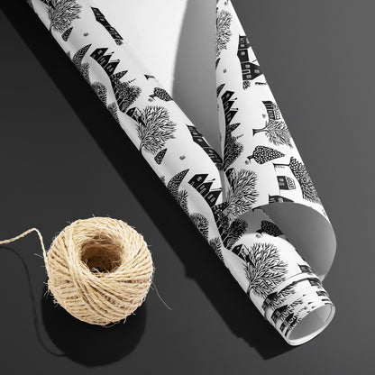 A partially unfurled Snowbound Village roll with its white underside beside a spool of natural twine on dark gray, showing black cottages and snowy trees on white.\