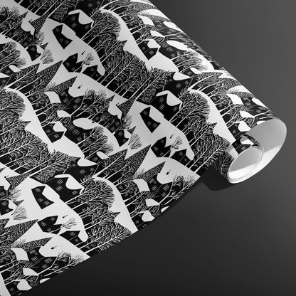 A partially unfurled roll of Snowy Silhouette displays snowy cottage and forest silhouettes in crisp black and white against a charcoal gray background.