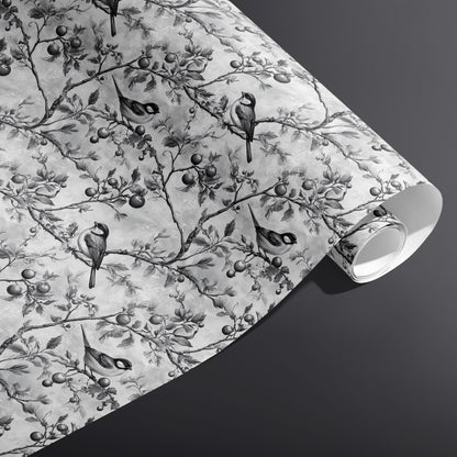 A partially unfurled roll of Winter Orchard wrapping paper showing monochrome birds and orchard branches on a misty gray ground against a dark charcoal background.