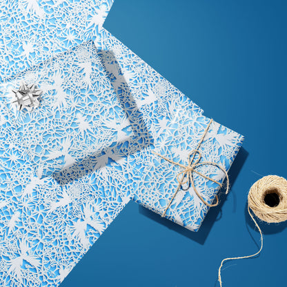 Two gifts in Winter's Whisper—one with a silver bow and one tied with twine—sit on two unused sheets with white lace winter florals on icy blue, on a deep blue surface beside twine.