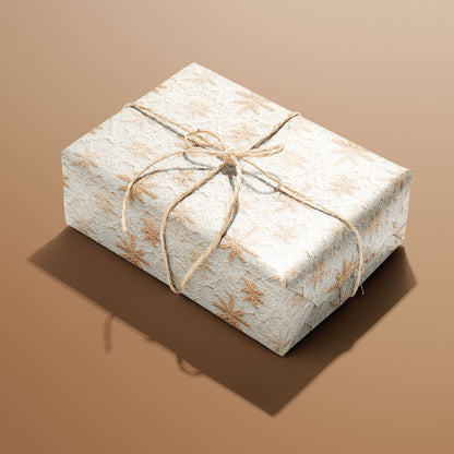 A single rectangular gift wrapped in Hygge Holiday and tied with natural twine, the tan knit snowflakes crisp on soft white against a caramel-brown background.