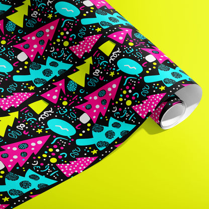 A partially unfurled roll of Neon Noel wrapping paper showing neon geometric trees and playful confetti marks on deep black against an acid-yellow background.