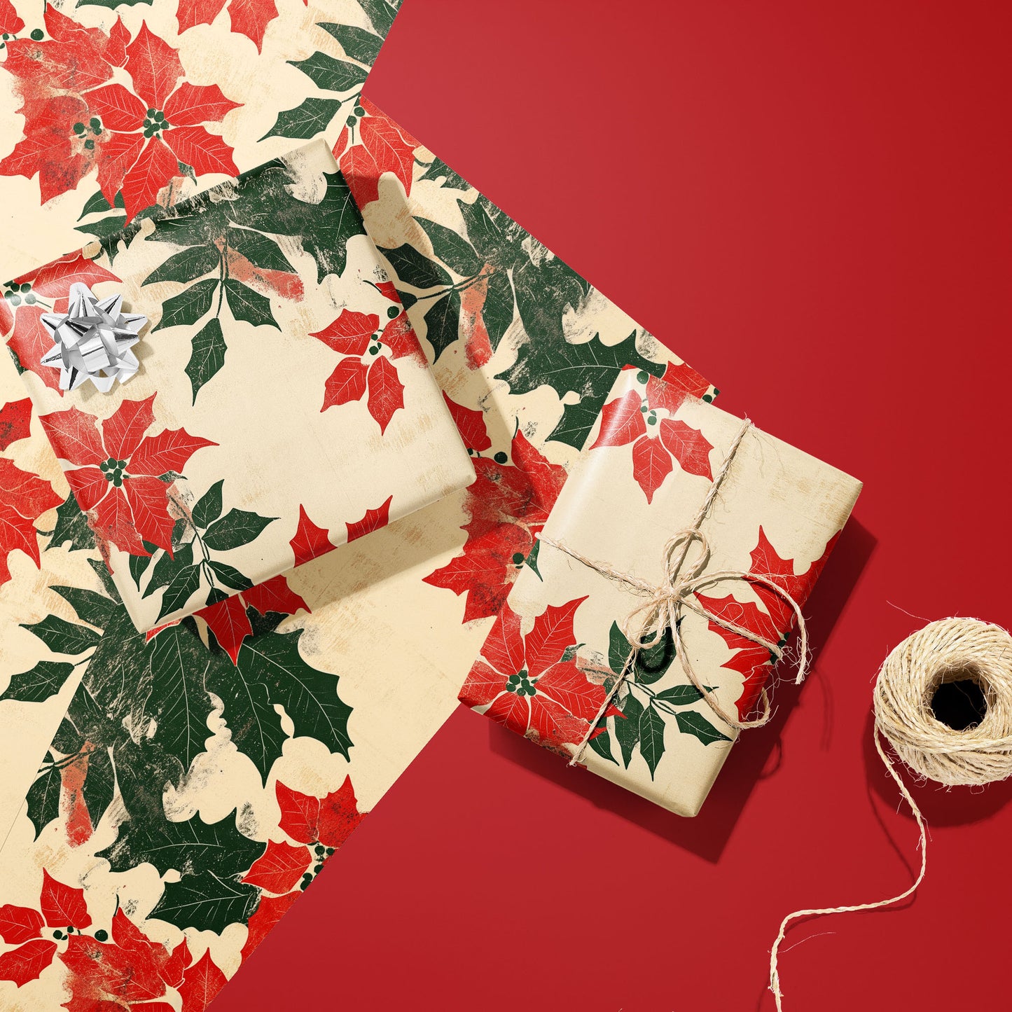 Two gifts wrapped in Woodblock Poinsettias floral paper, one with a silver bow and one tied with twine, resting on extra sheets beside twine on a red surface.