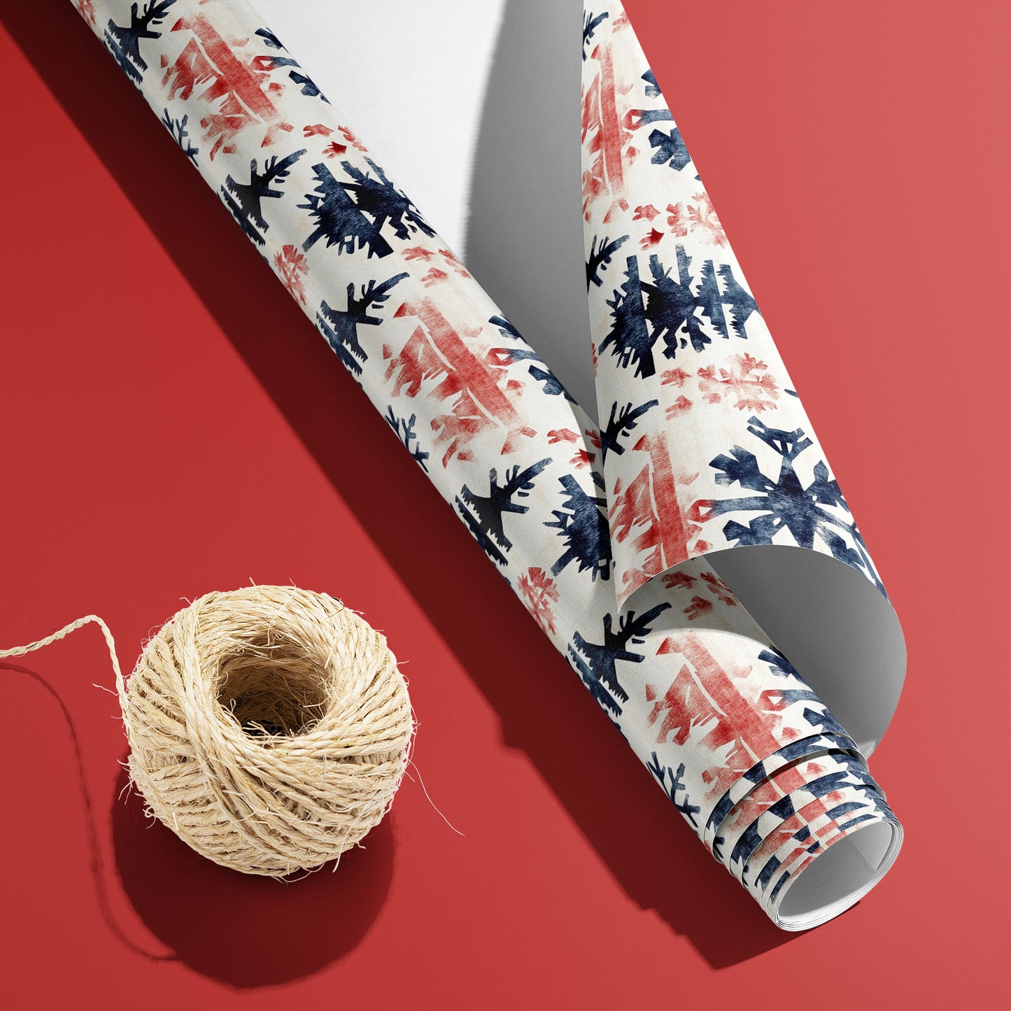 A curled roll of Scandinavian Snowflakes wrapping paper revealing its white underside beside a spool of natural twine on a rich red background.