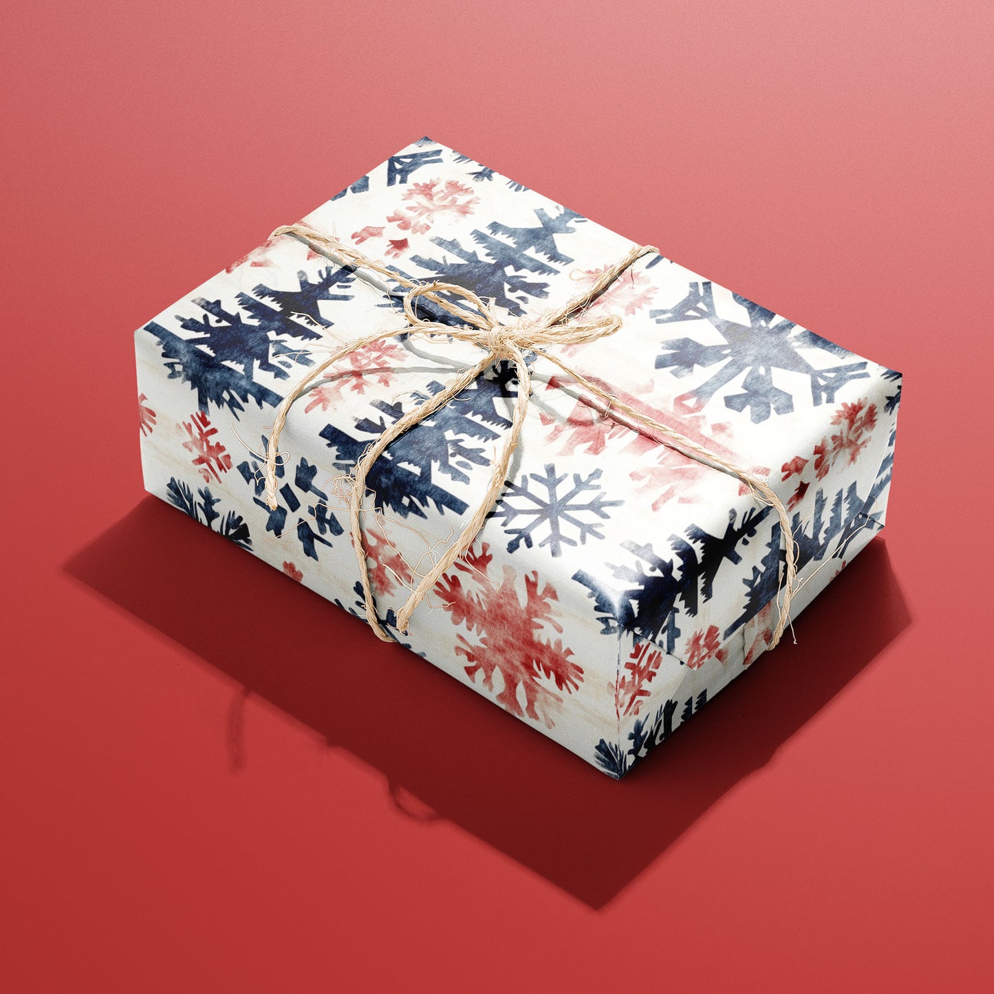 A single box wrapped in Scandinavian Snowflakes paper, patterned with navy and red snowflakes and trees and tied with rustic twine on a red backdrop.