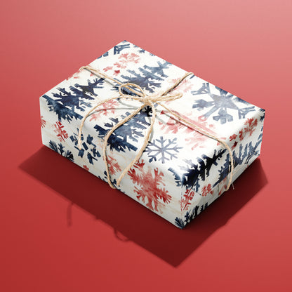 A single box wrapped in Scandinavian Snowflakes paper, patterned with navy and red snowflakes and trees and tied with rustic twine on a red backdrop.