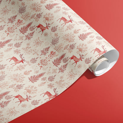 A partially unfurled roll of Nordic Wonderland gift wrap showing red reindeer and winter botanicals on cream paper against a warm red surface.